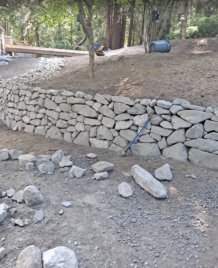 Dry-stacked stone retaining wall holding back a wooded slope