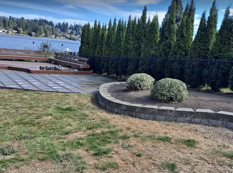 Waterfront paver patio with a curved block planter wall and clipped shrubs