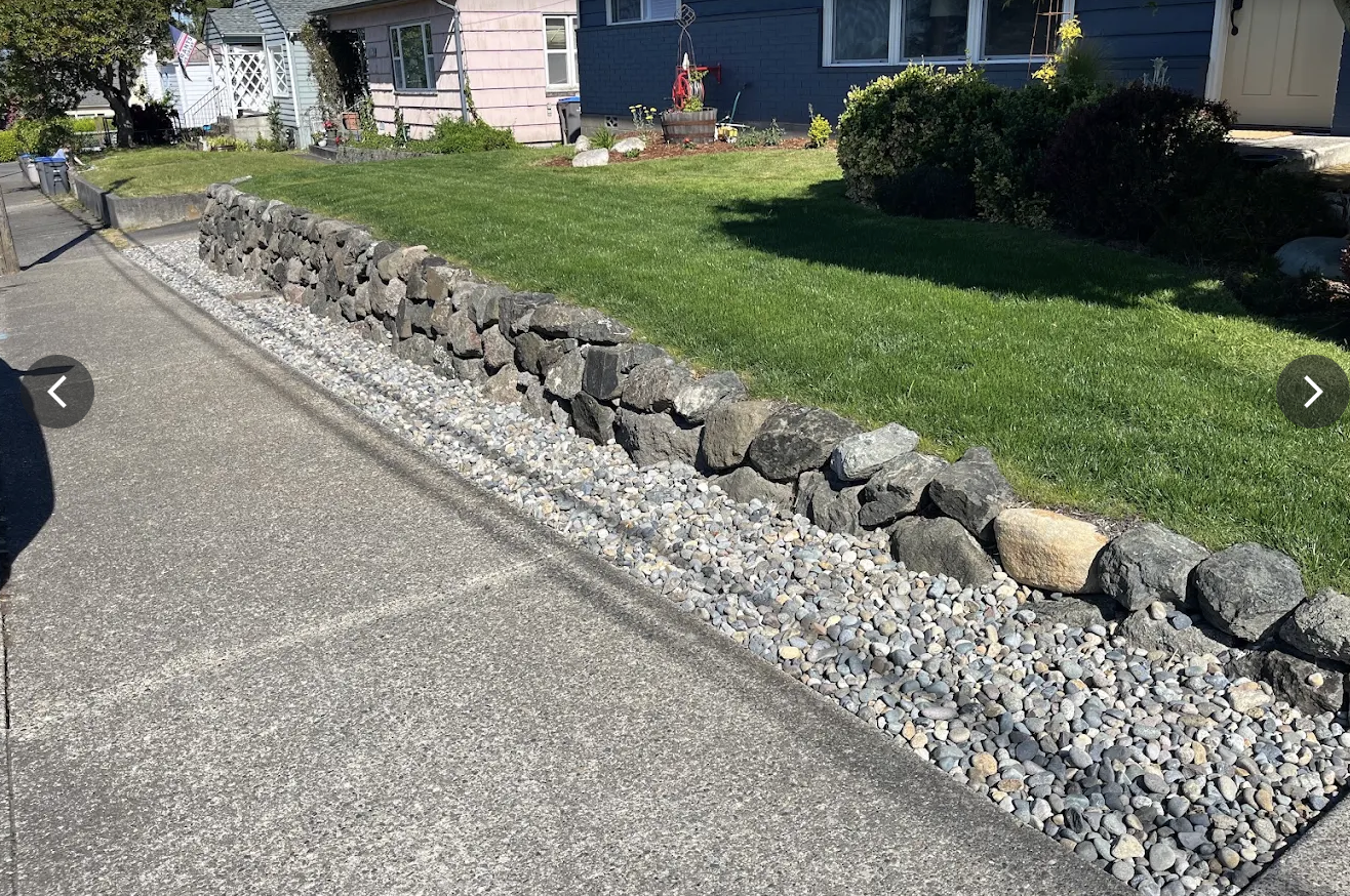 Stacked basalt rock wall along a driveway with a river rock drainage strip