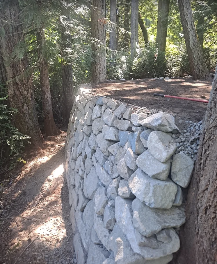 Hand-stacked stone wall with gravel backfill along a wooded trail